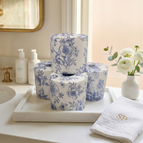 Bathroom counter with blue and white toile patterned toilet paper rolls, a towel, and a vase with flowers.
